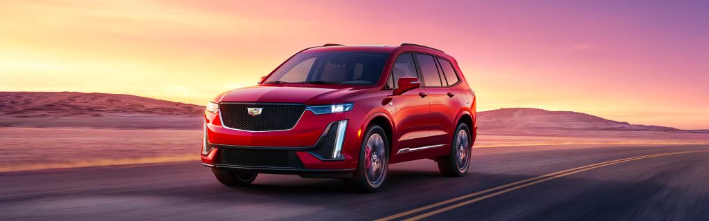 Red Cadillac XT6 driving on an open desert highway at sunset with a colorful sky in the background