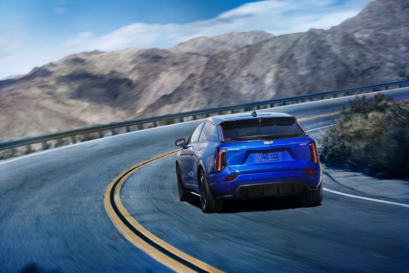Rear View of a Blue 2026 OPTIQ-V Driving on a Curve of a Mountain Row | Alexander Cadillac in Oxnard CA