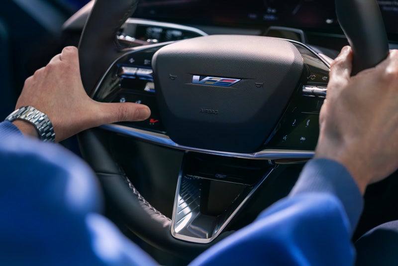 Close-up of a Man About to Press the V-Button on the 2026 OPTIQ-V Steering Wheel | Alexander Cadillac in Oxnard CA